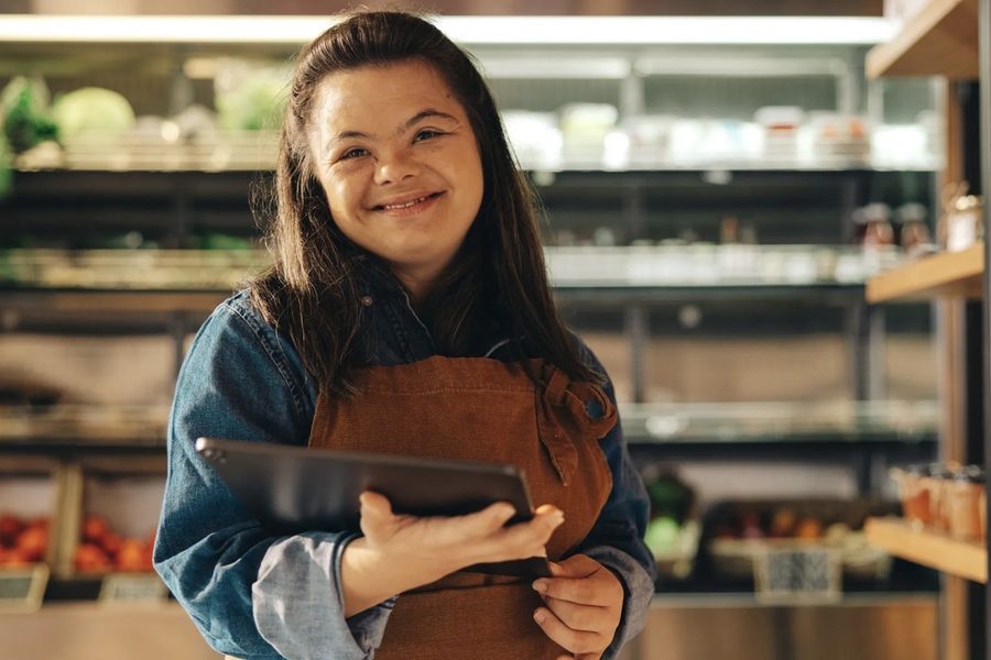 A participant in a work apron uses a tablet while working in a grocery store